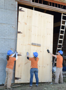 Three corps members hold up a new door on the barn